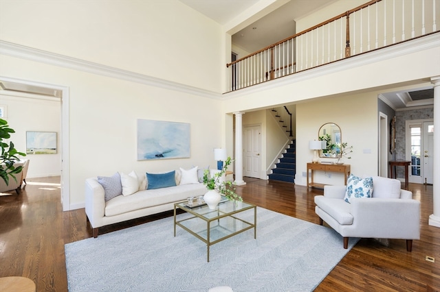 living room featuring dark hardwood / wood-style floors, a towering ceiling, crown molding, and ornate columns