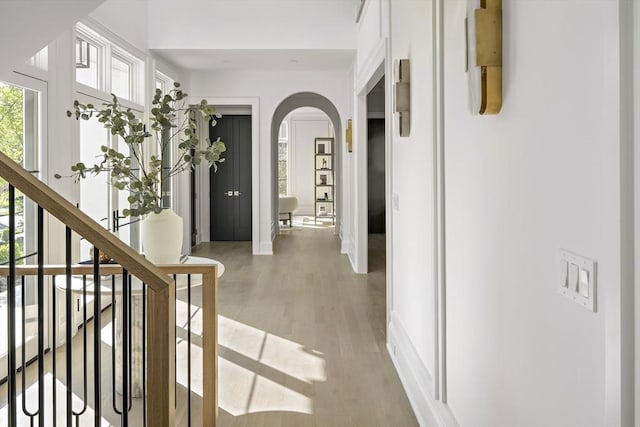 hall with stairway, light wood-style flooring, arched walkways, and baseboards