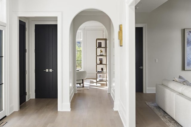 corridor with arched walkways, light wood-style floors, and baseboards
