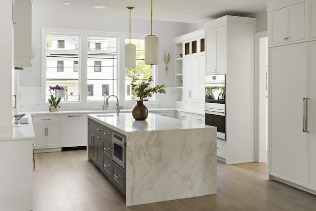 kitchen with an island with sink, a sink, open shelves, stainless steel appliances, and light wood-style floors