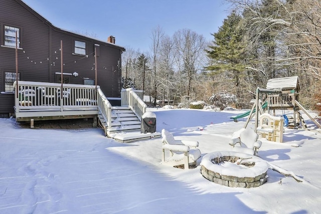 yard covered in snow featuring a deck, a fire pit, and a playground