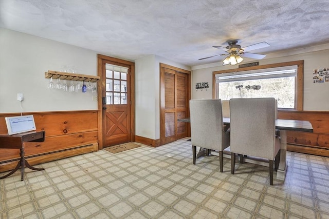 dining area featuring a textured ceiling, ceiling fan, wood walls, and a baseboard radiator