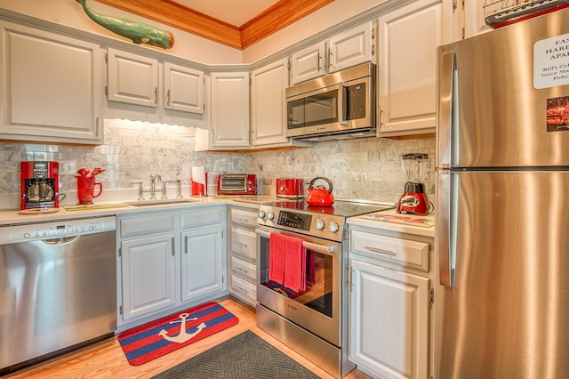 kitchen with light wood-type flooring, stainless steel appliances, backsplash, sink, and crown molding