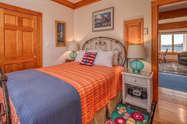 bedroom with a water view, ornamental molding, and light hardwood / wood-style floors