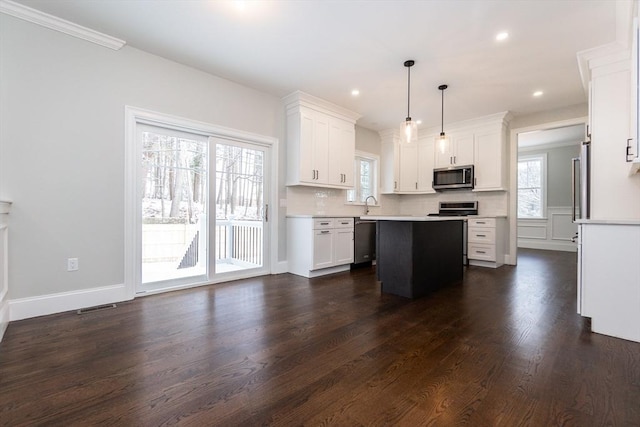 kitchen featuring hanging light fixtures, a kitchen island, a wealth of natural light, stainless steel appliances, and white cabinets