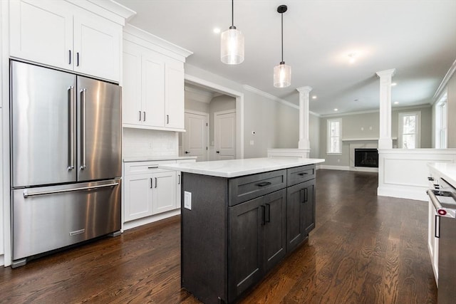 kitchen with ornate columns, appliances with stainless steel finishes, white cabinetry, hanging light fixtures, and ornamental molding