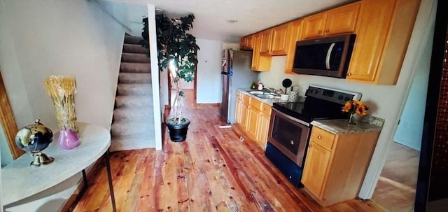 kitchen featuring stainless steel appliances, light countertops, a sink, and light wood-style flooring