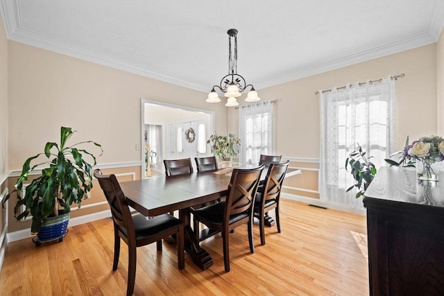 dining space with crown molding, an inviting chandelier, and light hardwood / wood-style flooring