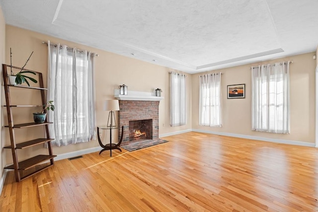 unfurnished living room featuring a fireplace, a raised ceiling, and light hardwood / wood-style flooring