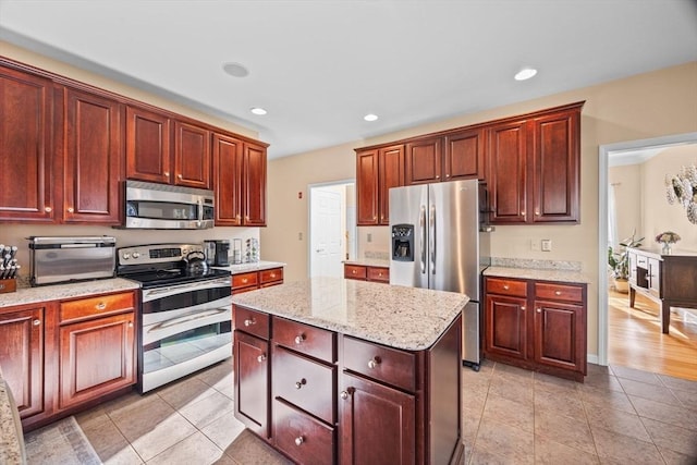 kitchen featuring light tile patterned floors, a kitchen island, light stone countertops, and appliances with stainless steel finishes