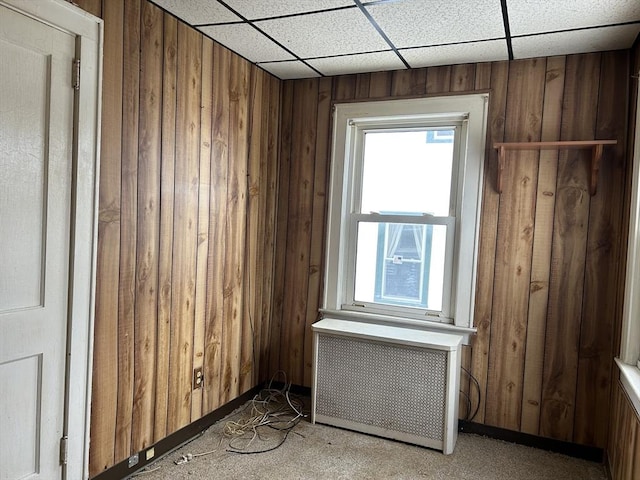 unfurnished room with radiator heating unit, a drop ceiling, and wood walls