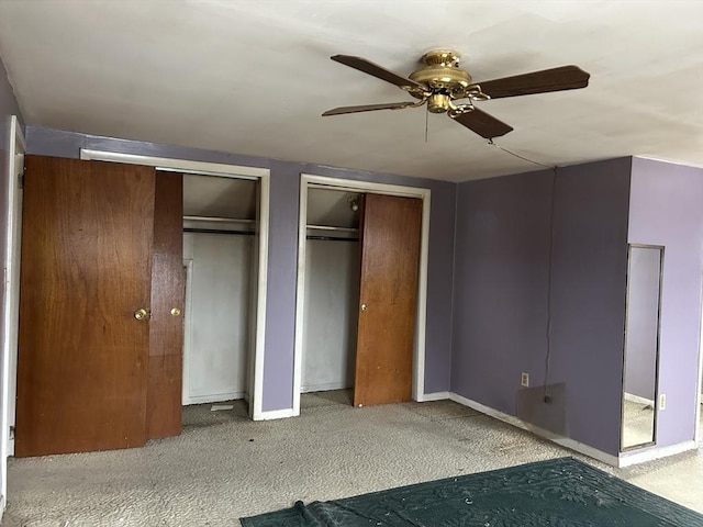 unfurnished bedroom with ceiling fan, light carpet, and two closets