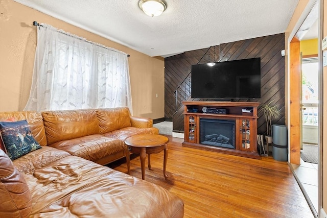living room featuring wood walls, wood finished floors, a textured ceiling, a fireplace with raised hearth, and an accent wall