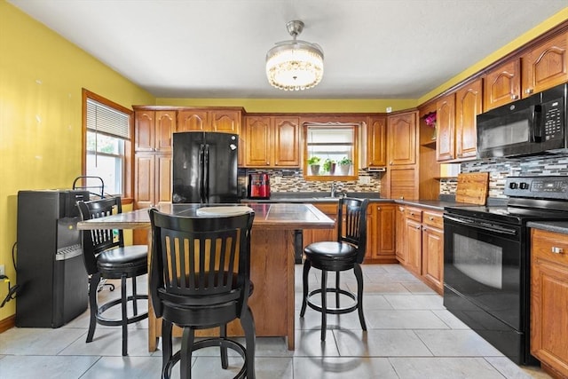 kitchen with black appliances, a kitchen bar, a center island, and brown cabinetry