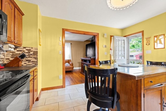 kitchen featuring black appliances, brown cabinetry, backsplash, baseboards, and light tile patterned flooring