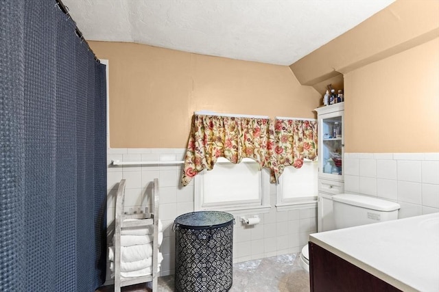 full bath with tile walls, wainscoting, toilet, and vanity