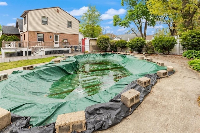 view of swimming pool featuring a deck, a fenced backyard, a storage unit, and an outdoor structure