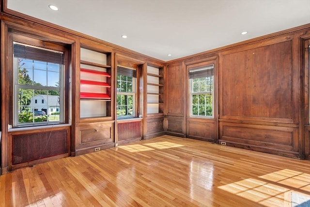 empty room featuring ornamental molding, recessed lighting, wood walls, and light wood finished floors