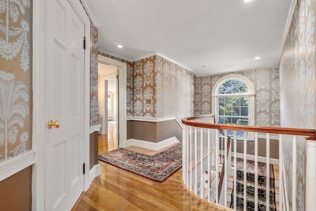 corridor with crown molding, wood finished floors, an upstairs landing, and wallpapered walls