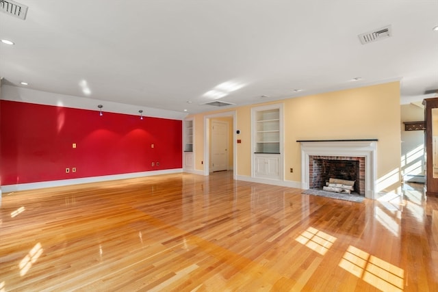 unfurnished living room with built in shelves, light hardwood / wood-style flooring, and a brick fireplace