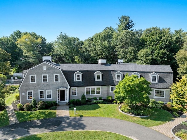 view of front of home featuring a front yard, a chimney, and a gambrel roof