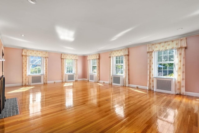 unfurnished living room featuring baseboards, radiator heating unit, and light wood-style floors