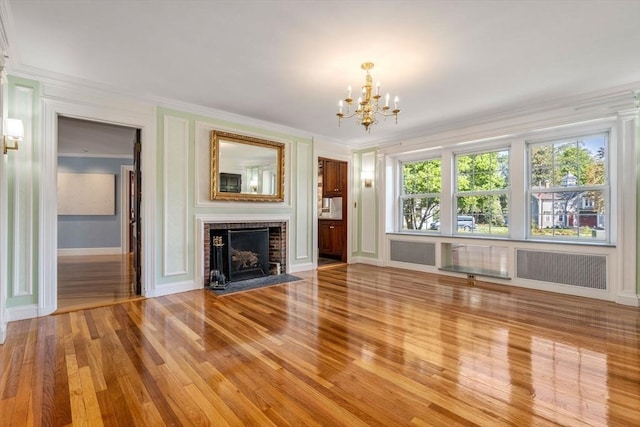 unfurnished living room with a brick fireplace, a notable chandelier, crown molding, and light wood finished floors