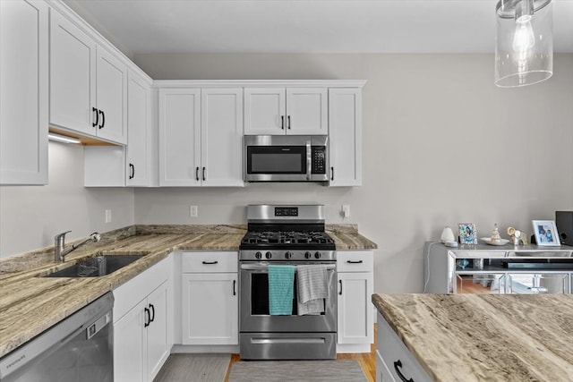 kitchen with a sink, light stone countertops, appliances with stainless steel finishes, and white cabinets