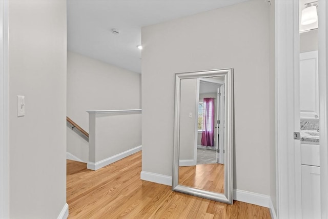 hallway featuring an upstairs landing, baseboards, and light wood-style floors