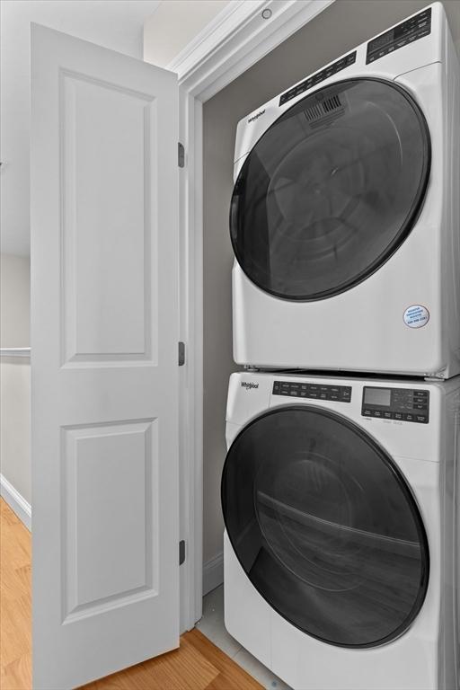 clothes washing area featuring laundry area, stacked washer and clothes dryer, and light wood finished floors