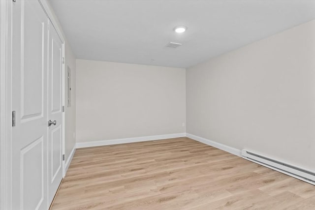 spare room featuring a baseboard heating unit, light wood-style floors, and baseboards