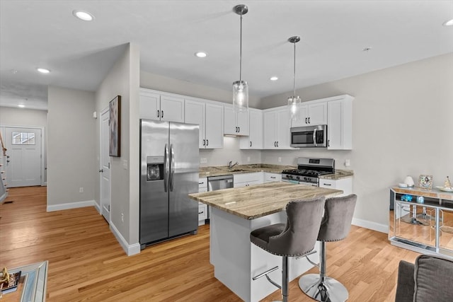 kitchen featuring light stone counters, white cabinetry, appliances with stainless steel finishes, light wood finished floors, and hanging light fixtures