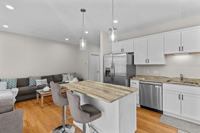 kitchen with a sink, light wood-style floors, appliances with stainless steel finishes, white cabinetry, and open floor plan