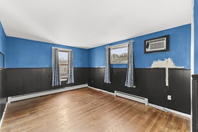 unfurnished room featuring a baseboard heating unit, a wall unit AC, and hardwood / wood-style flooring