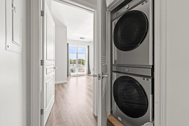 laundry room with laundry area, visible vents, stacked washer / drying machine, light wood-type flooring, and baseboards