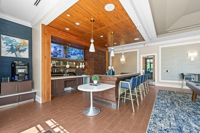 bar with crown molding, hanging light fixtures, baseboards, wallpapered walls, and wood finished floors