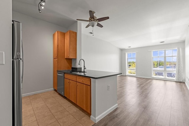 kitchen with a peninsula, lofted ceiling, dark countertops, a sink, and appliances with stainless steel finishes