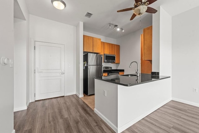 kitchen with dark countertops, a sink, stainless steel appliances, a ceiling fan, and wood finished floors