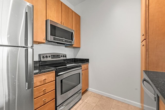 kitchen featuring appliances with stainless steel finishes, brown cabinets, light tile patterned floors, baseboards, and dark stone countertops