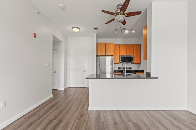 kitchen featuring brown cabinetry, appliances with stainless steel finishes, wood finished floors, and ceiling fan
