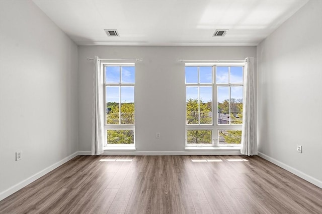 empty room featuring baseboards, wood finished floors, and visible vents