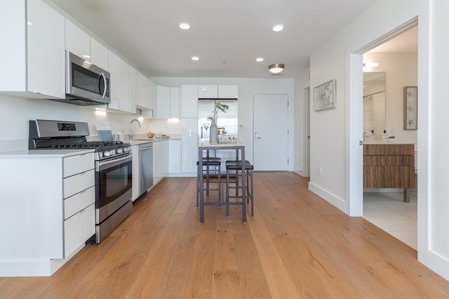 kitchen featuring light wood finished floors, a sink, appliances with stainless steel finishes, white cabinets, and light countertops