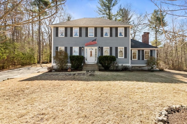 colonial inspired home featuring entry steps, a front yard, roof with shingles, and a chimney