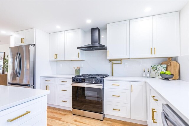 kitchen featuring wall chimney range hood, light hardwood / wood-style flooring, white cabinets, and appliances with stainless steel finishes