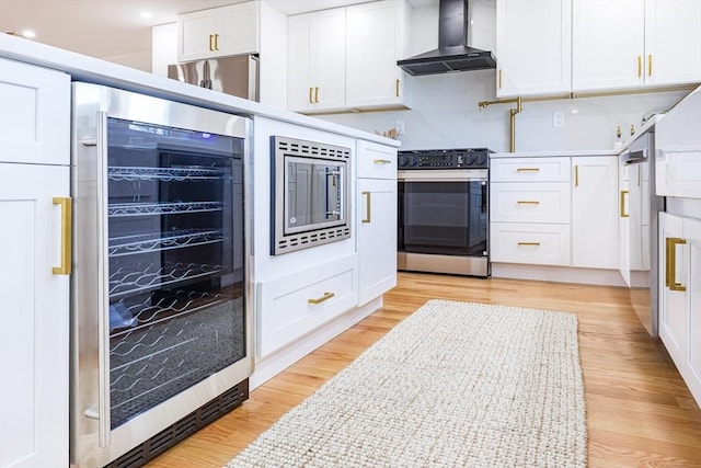 kitchen with appliances with stainless steel finishes, white cabinetry, light hardwood / wood-style floors, beverage cooler, and wall chimney exhaust hood