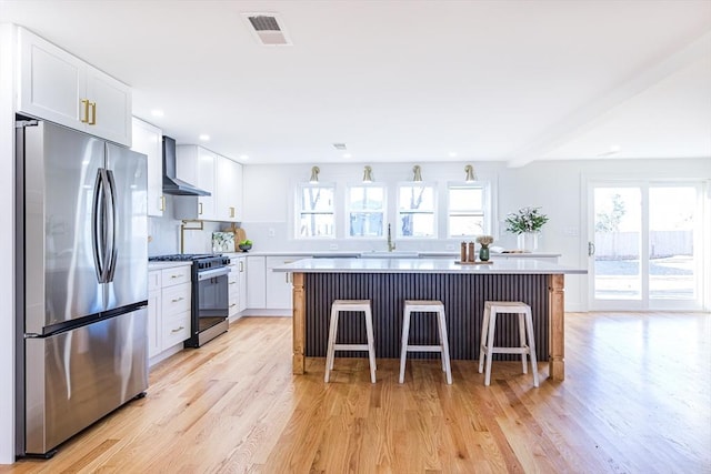 kitchen with light hardwood / wood-style flooring, appliances with stainless steel finishes, a center island, white cabinets, and a kitchen bar