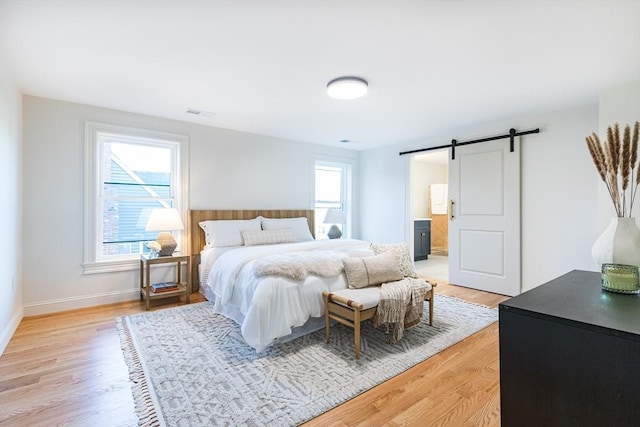 bedroom featuring a barn door, connected bathroom, and light hardwood / wood-style flooring