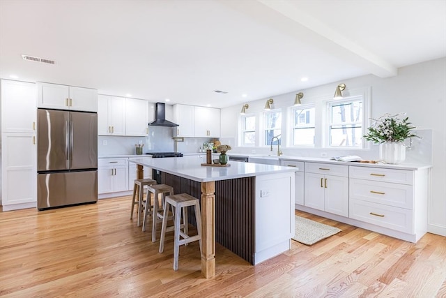 kitchen featuring white cabinetry, stainless steel refrigerator, wall chimney exhaust hood, and a kitchen island