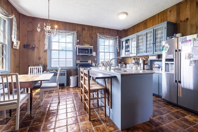 kitchen with kitchen peninsula, appliances with stainless steel finishes, a chandelier, wooden walls, and pendant lighting