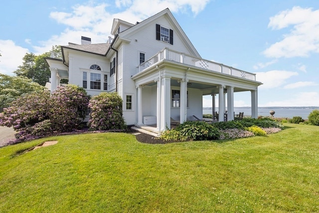 rear view of property featuring a balcony, a lawn, and a water view